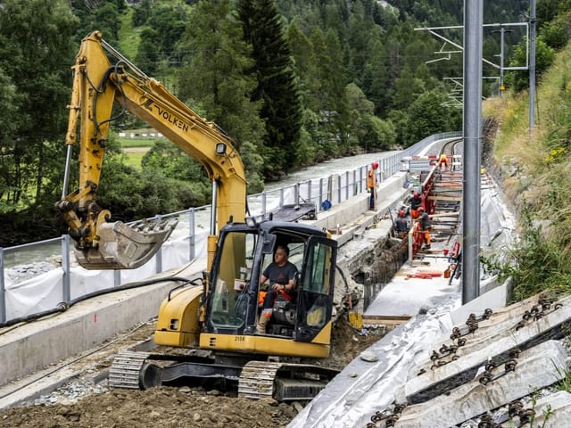 Bauarbeiter und Bagger auf einer Bahnbaustelle in den Bergen.