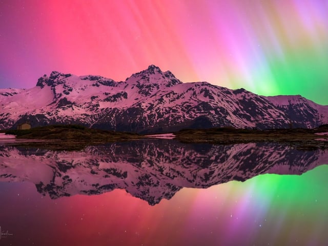 Nordlichter über schneebedeckten Bergen mit Spiegelung im Wasser