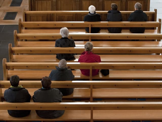 Menschen sitzen hinten in einer Kirche.