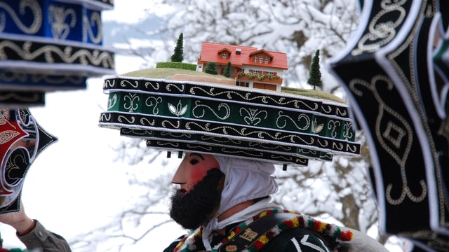 Eine Person mit farbenfroher Haube und Maske.