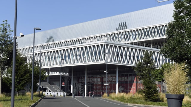 Moderne Fassade eines Gebäudes mit geometrischem Muster und Vordach, eine Strasse im Vordergrund.