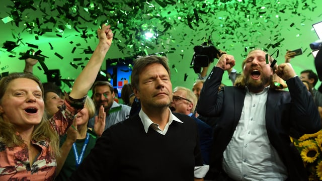 Habeck steht mit geschlossenen Augen neben jubelnden Parteikollegen, von der Decke regnen in grünem Licht grüne Glitzerschnipsel.