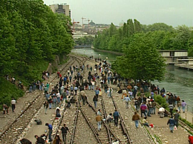 Menschen auf Zuggeleise neben der Limmat. Die offene Drogenszene am Letten.