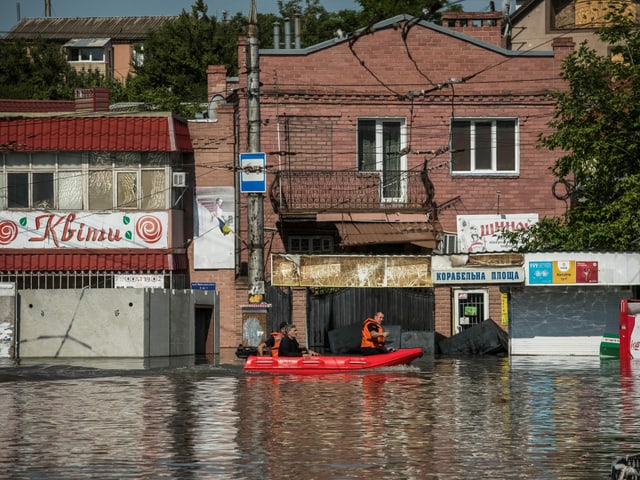 Eine Strasse ist überflutet. Auf dem Wasser fährt ein rotes Schlauchboot.