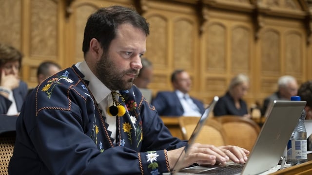 Ein Mann in einem mit Blumen bestickten Hemd arbeitet an einem Laptop.