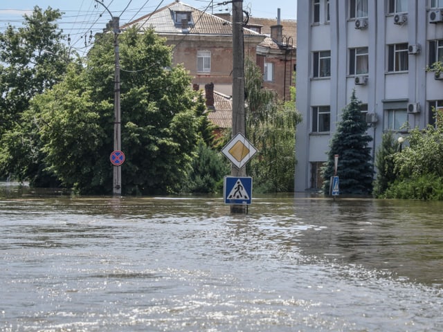 Blick auf eine überflutete Strasse. Das Wasser reicht fast bis zu den Strassenschildern an einem Pfosten.