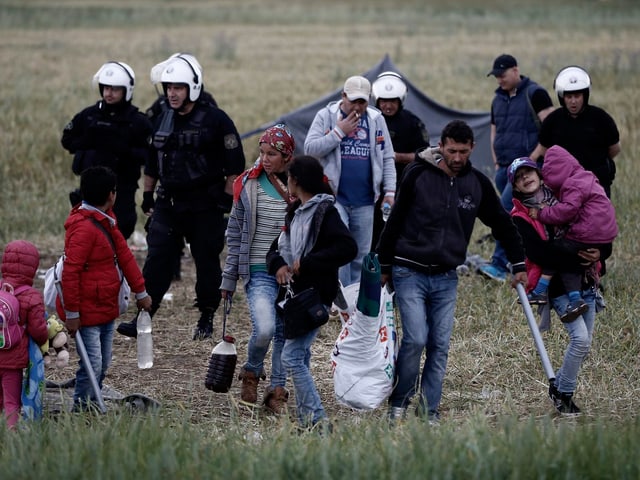 Personen mit Gepäck welche von Polizisten begleitet werden.