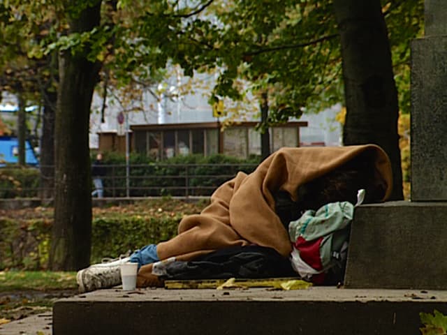 Verwahrloster Junkie am Platzspitz, eingehüllt in eine Decke, nur die Füsse schauen heraus.