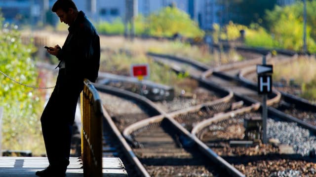 Mann an Geländer lehnend neben leeren Geleisen