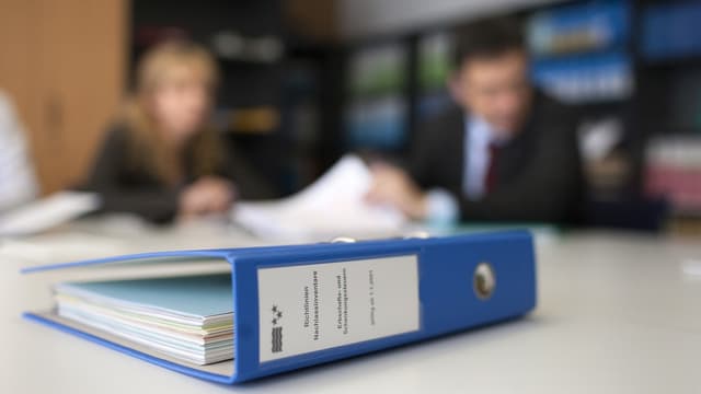 Ordner auf dem Tisch, im Hintergrund Menschen, bei der Finanzverwaltung des Kantons Aargau