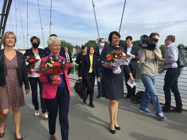 Dreis Frauen marschieren gemeinsam, hinter ihnen ist Publikum und daneben ein Kameramann.