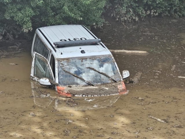 Polizeiauto zur Hälfte in dreckigem hellbraunem Wasser versunken, Türe halb offen.