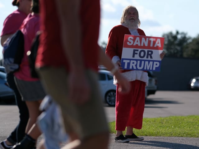 A Trump supporter dressed as Santa Claus holding a Santas for Trump poster.