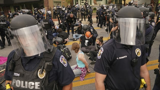 Protesters with their hands tied sit on the ground