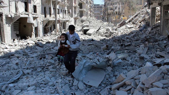 Kein Stein mehr auf dem anderen in Aleppo. Ein Mann trägt ein Mädchen über Trümmer.