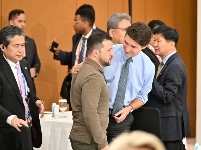 Trudeau legt Selenski die Hand auf die Schulter und lächelt ihn an.