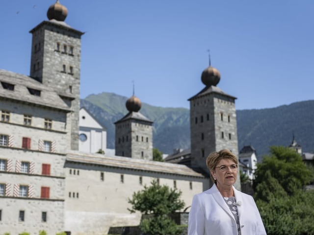 Frau vor historischer Burg mit drei Türmen und Bergen.