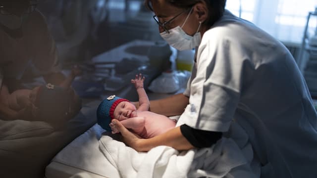 Die Hebamme trägt eine Maske, das Baby eine gestrickte Mütze.