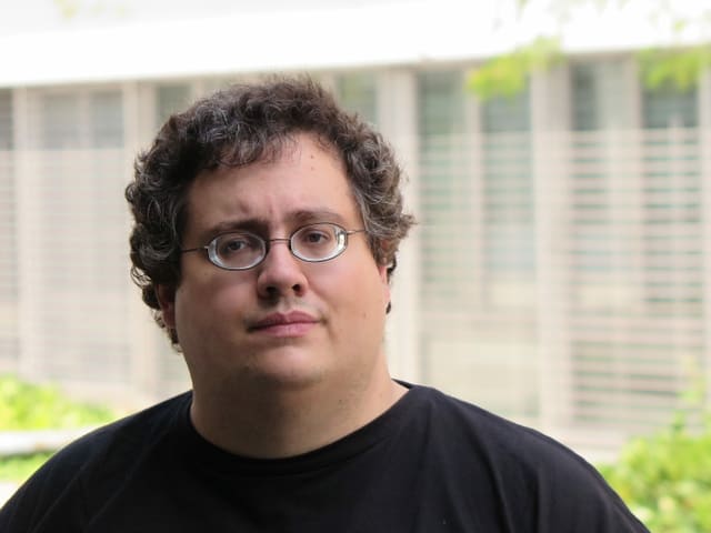 Ein Mann mit Locken, Brille und schwarzem Shirt.