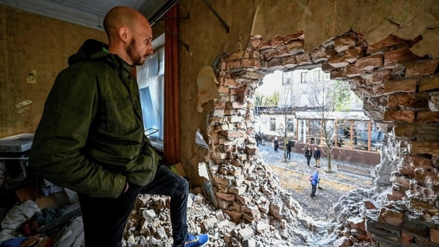 Ein Mann schaut aus einem Loch in der Wand auf die Strasse. Das Loch wurde von einer Rakete verursacht.