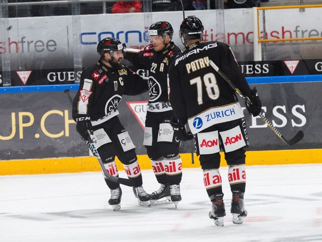 Drei Eishockeyspieler in schwarzen Trikots beim Feiern auf dem Eis.