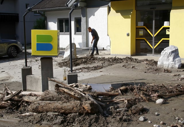 Ein Mann mit der Schaufel scheint das auf der Strasse liegende Geröll neben einem Haus wegzutragen.