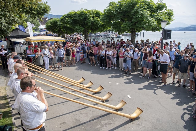 Gruppe von Alphornspielern spielt vor Zuschauern am Zugersee.