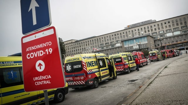 Ambulances wait in a long line in front of a hospital.