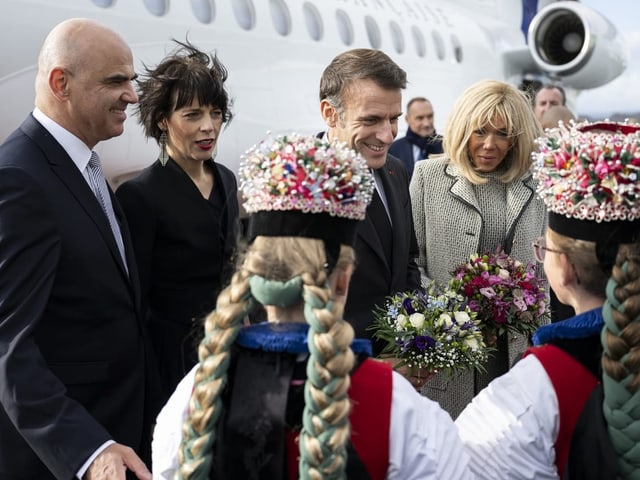 Zwei Mädchen in Trachten, die Bersets und die Macrons stehen vor einem Flugzeug.