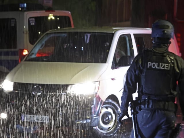 Polizist in der Nacht bei Regen vor einem Polizeifahrzeug.