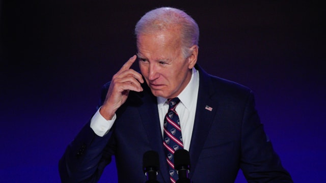 Biden tippt sich mit dem Zeigefinger an die Stirn.