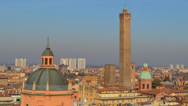 Ein Stadt mit einem hohen Turm und mehreren Kuppeln und alten Häusern. Viele davon rot.