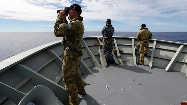 Männer mit Feldstecher schauen vom Schiff aufs Meer.