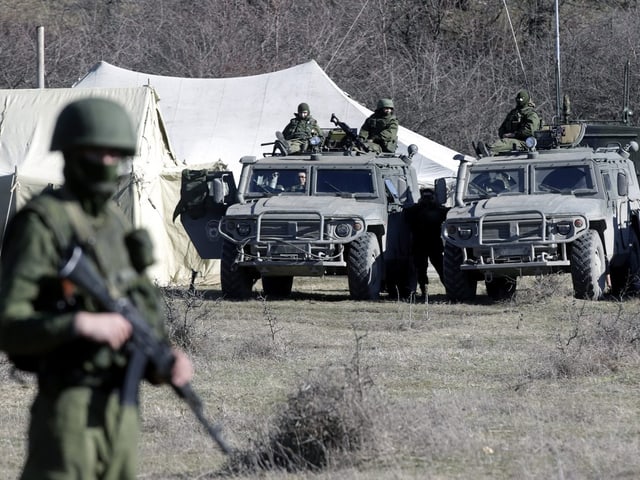 Bewaffnete Männer und Militärfahrzeuge auf einer Wiese.