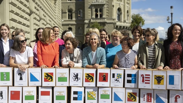 Etwa 20 Frauen posieren vor dem Bundeshaus hinter einer Theke, worauf alle Kantonswappen auf Papier angeklebt sind.