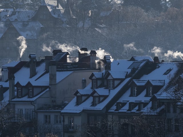 Winterliche Dächer mit Schornsteinen, aus denen Rauch steigt.