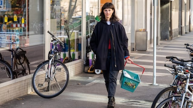 Junge Frau mit dunklen Haaren und Einkaufskorb in der Hand öffnet die Wohnungstür.