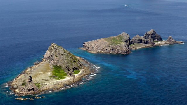 Zwei kleine Felseninseln, umgeben von blauem Meer, aufgenommen aus der Luft.