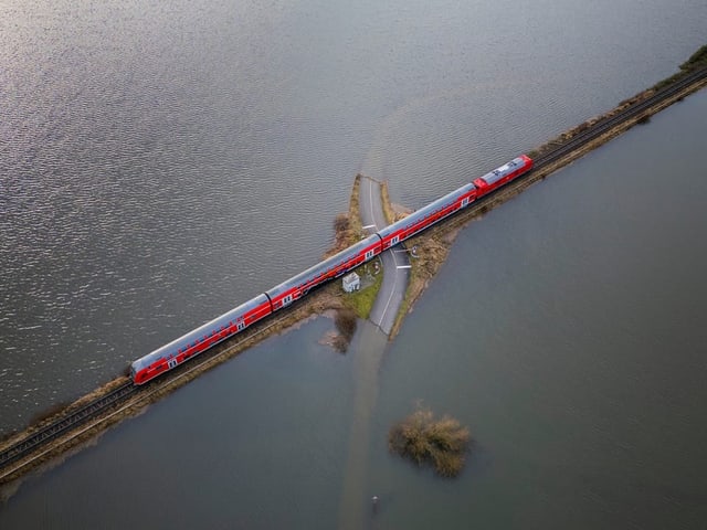 Ein Zug fährt durch eine von Hochwasser betroffenen Landschaft. Bild aus der Vogelperspektive.