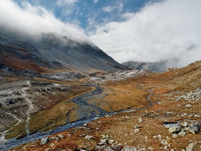 Blick über Hochebene mit Fluss in der Mitte, im Hintergrund Wolken über Berge