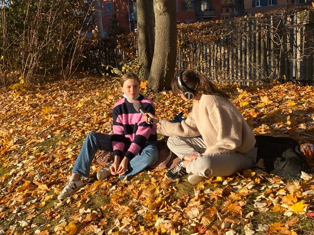 Reporterin Dania und Kinderreporterin Mathila sitzen auf dem Boden. 