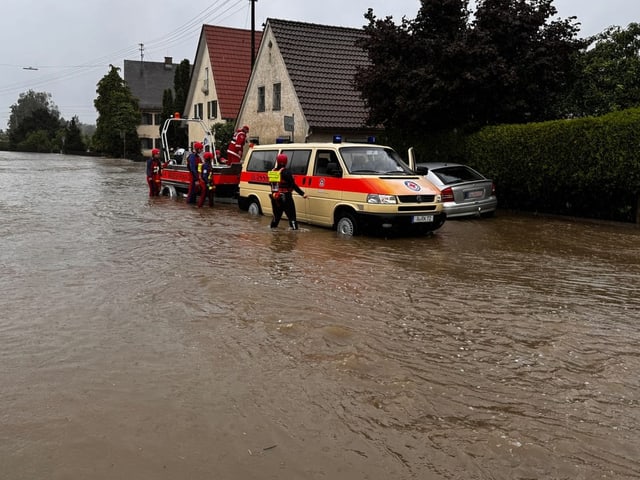 Rettungsfahrzeug und Einsatzkräfte bei Hochwasser auf einer Strasse.