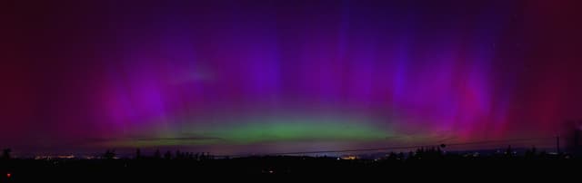 Rosaroter Himmel durch Polarlichter. Davor Silhouette der Landschaft.