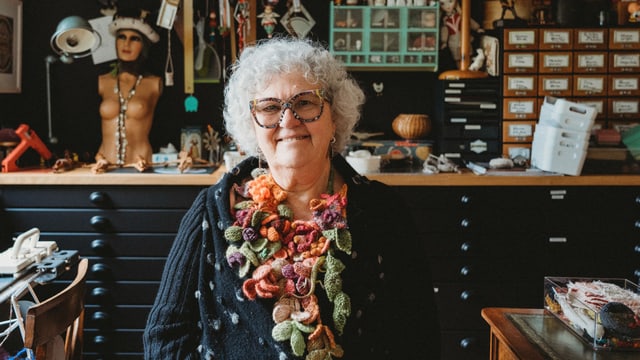 Madame Tricot in ihrem Atelier. Sie hat eine gestrickte Kette an.