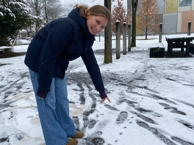 Mädchen steht im Schnee und zeigt auf Tierspuren