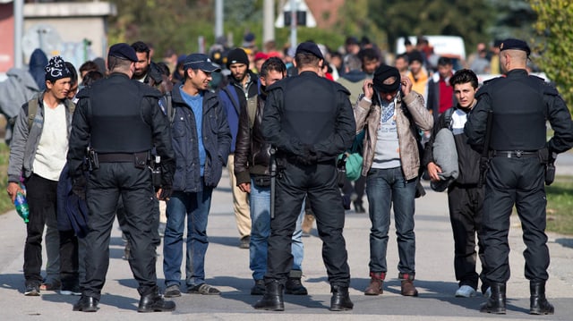 Männer stehen auf einer Strasse drei Polizisten gegenüber.