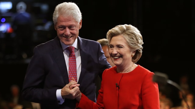 Bill und Hillary Clinton nach einer Wahlveranstaltung, halten sich die Hand und lächeln.