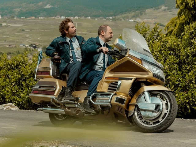 Zwei Männer in Uniform auf einem Motorrad.