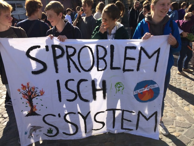 Vier Jungen mit einem Plakat und der Aufschrift: «S'Problem isch s'Syschtem.»