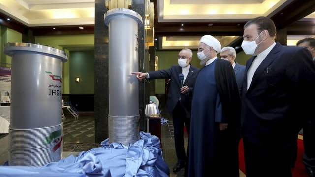 Männer mit Anzügen und mit weissen Masken stehen vor Rohren. Rohani trägt einen weissen Turban.